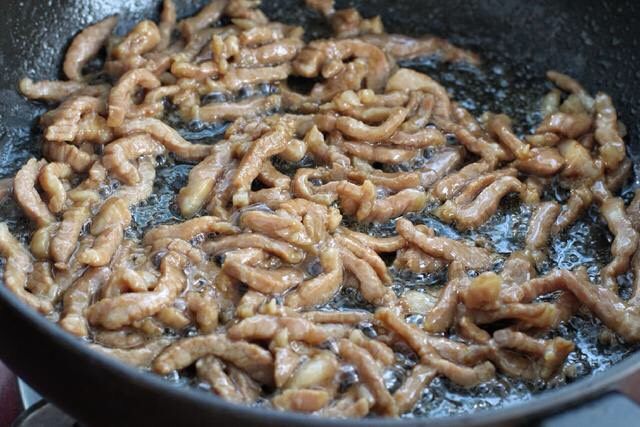 四季豆炒肉,锅中倒适量食用油烧热,放入腌制好的肉丝滑炒至变色断生状态盛出。