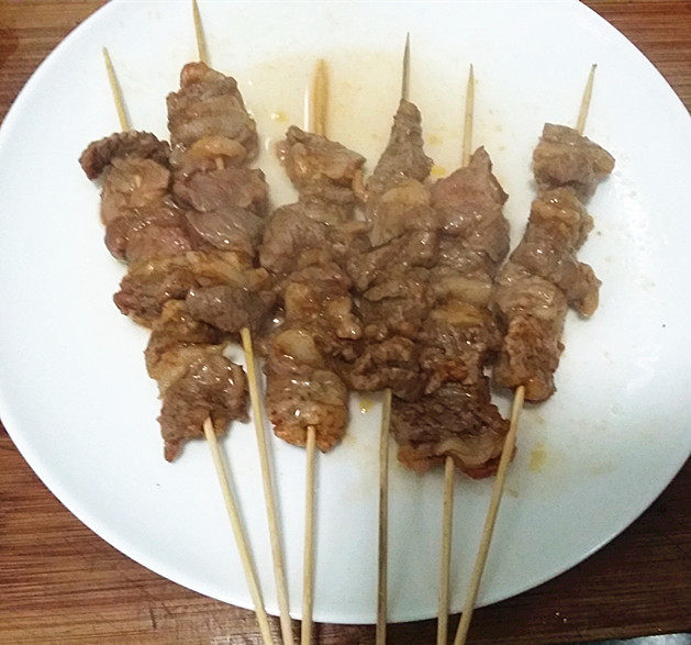 孜然羊肉串,取出倒掉烘烤出来的汁水,表面刷腌料汁后翻面