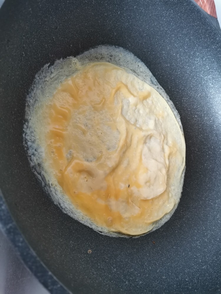 莴笋炒鸡蛋,晃动锅,让蛋液摊成一个圆饼。