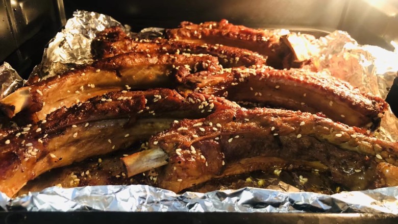 蒜香烤排骨,将烤盘包好锡纸,排骨摆放均匀,撒上白芝麻入烤箱烤5分钟,翻面撒上白芝麻继续烤5分钟,烤箱上火220度,下火180度