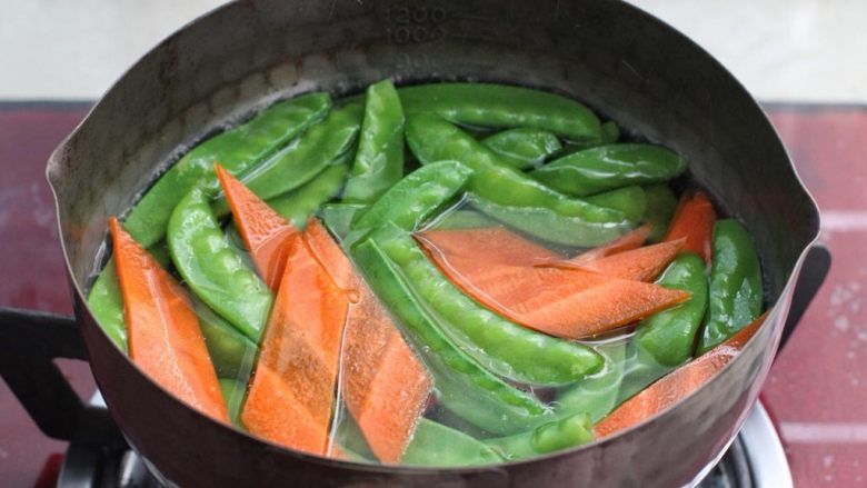 荷兰豆炒香肠,锅中添适量清水烧至沸腾,淋入几滴食用油和少许盐,放入荷兰豆和胡萝卜焯烫一分钟左右,捞出立刻过凉水沥干水分。