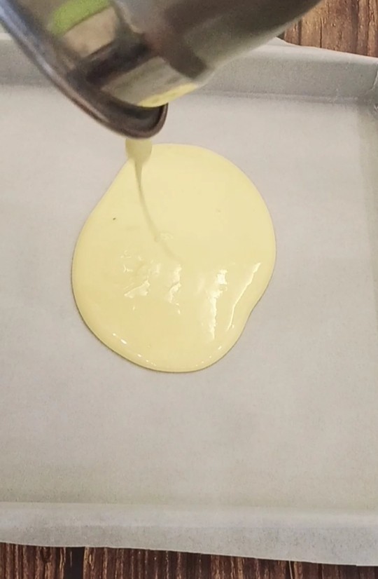 虎皮蛋糕卷,蛋黄糊倒入铺了油纸的四方烤盘中,用刮板刮平整。