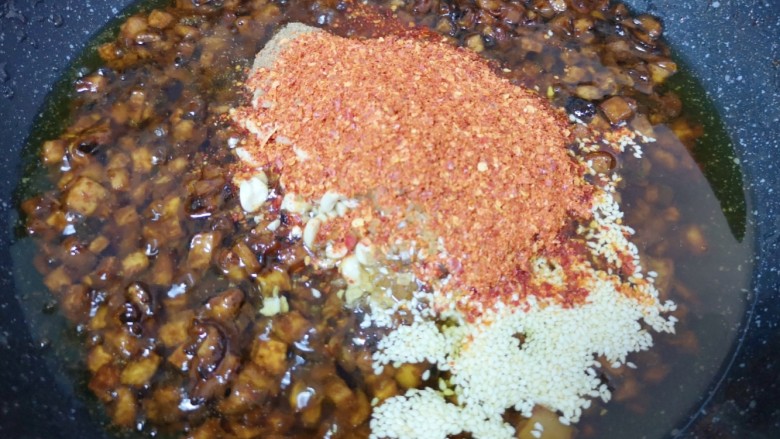 香菇牛肉酱,放入熟白芝麻、熟花生碎、五香粉、辣椒粉和冰糖碎,转小火炒至辣椒出红油,冰糖碎融化。