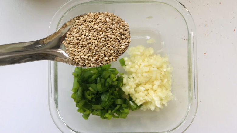 麻酱凉面,把刚才处理好的葱花蒜末放在耐热容器里,再加入一勺白芝麻;
