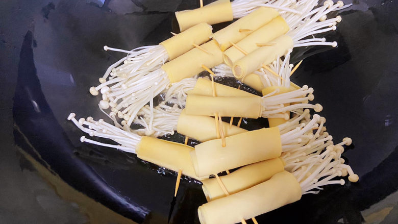 豆皮金针菇卷,锅中倒适量的油,油热改中小火,将金针菇放入锅中,两面都煎一下。