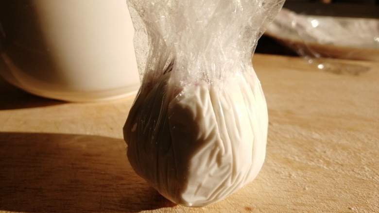紫薯芝麻饼,下面的保鲜膜向上包紧,打开保鲜膜,最顶端用手指整形一点一点收口。