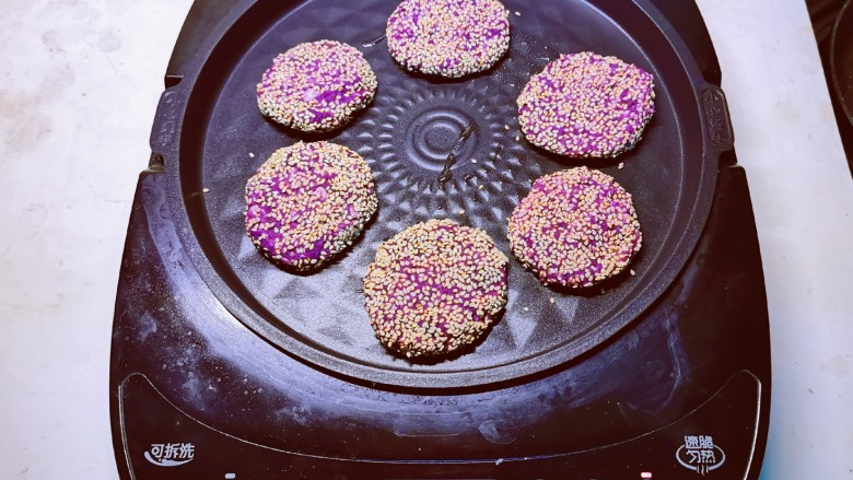 紫薯芝麻饼,煎烤机先预热刷油,将饼胚放入 煎至一面定型后翻另一面。