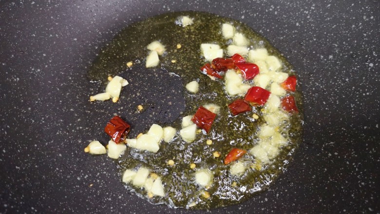 毛豆烧茄子,炒锅内倒适量的食用油烧热,下入大蒜和干红辣椒炒香。