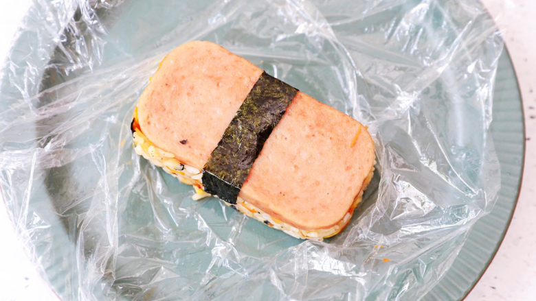 午餐肉饭团,最后将保鲜膜提出,取出饭团,再包上一条海苔即可
