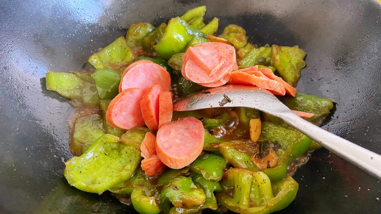 青椒炒香肠,锅中的水差不多炒干了,加一点点盐,把香肠片倒入锅中翻炒。