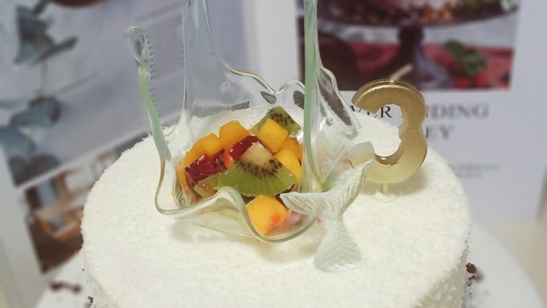 艾素糖造型水果蛋糕,抹面不用非常平整,因为蛋糕底部粘了一层奥利奥碎,其余部分粘了一层椰蓉,看起来有颗粒感,更像是白色的沙滩。把艾素糖排在大面上,再放些水果丁,就完成了。