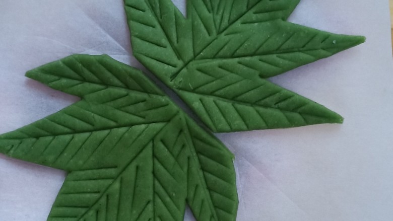 紫薯小馒头(葡萄馒头),取绿色面团,擀成薄片,用刀切出叶子的轮廓,再把叶片的纹路压出来。做4片,流出一丢丢的绿色面团搓成1毫米粗的细条作为藤