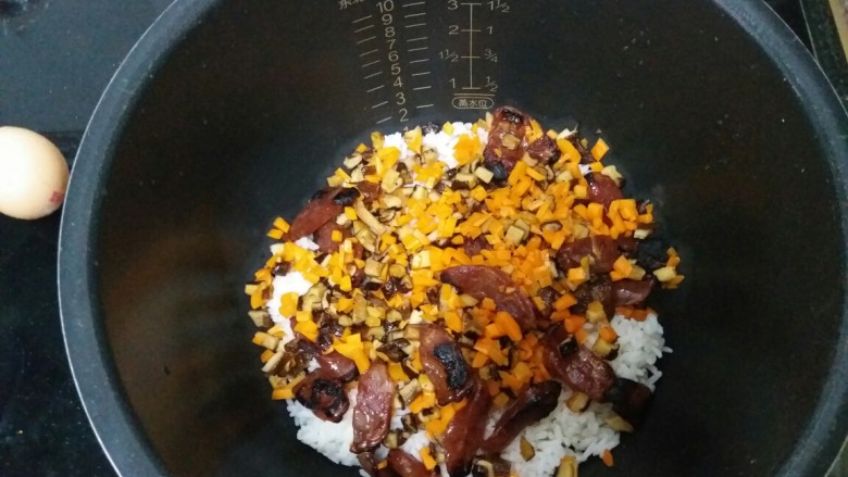 电饭煲腊肠饭,将炒好的腊肠,胡萝卜和香菇放入电饭煲中