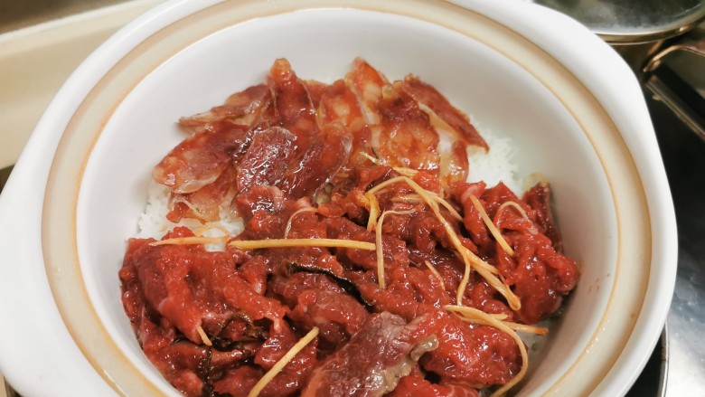 广式煲仔饭,饭表面均匀铺上肉肉,加盖小火继续焗7-8分钟。中途要不时移动煲底受热位置,等火力均匀,饭和肉肉焗着味道互相渗透。