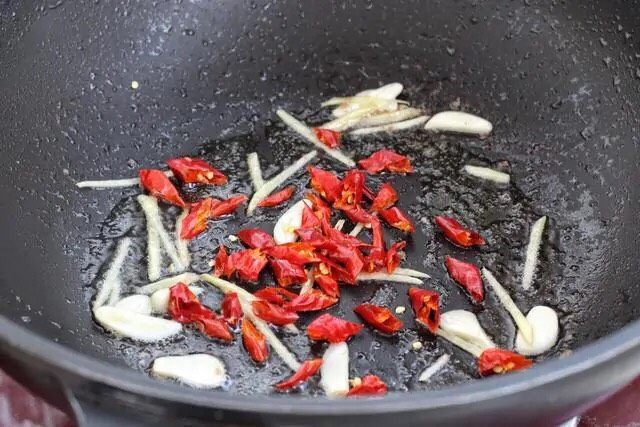小炒牛肉,就着锅中底油放入姜丝、蒜片和红干椒,小火炒出香味。