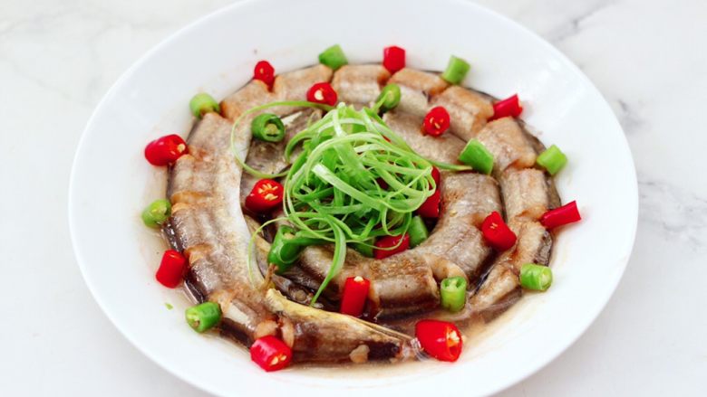 风味双椒蒸海鳗,蒸好的海鳗取出,把葱姜丝捡出不用,摆上小米辣和青尖椒,撒上葱丝。