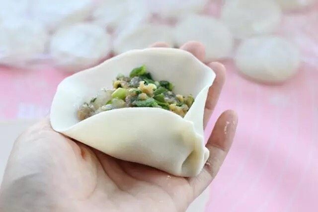 三鲜蒸饺,取一张饼皮在中间放上馅料,然后包成饺子形状。