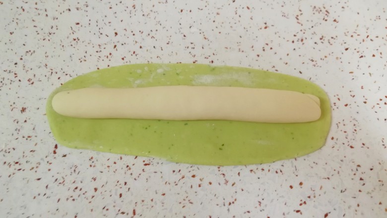 猪肉白菜水饺,白色的长条状面团放在绿色的长方形面团上,卷起来。