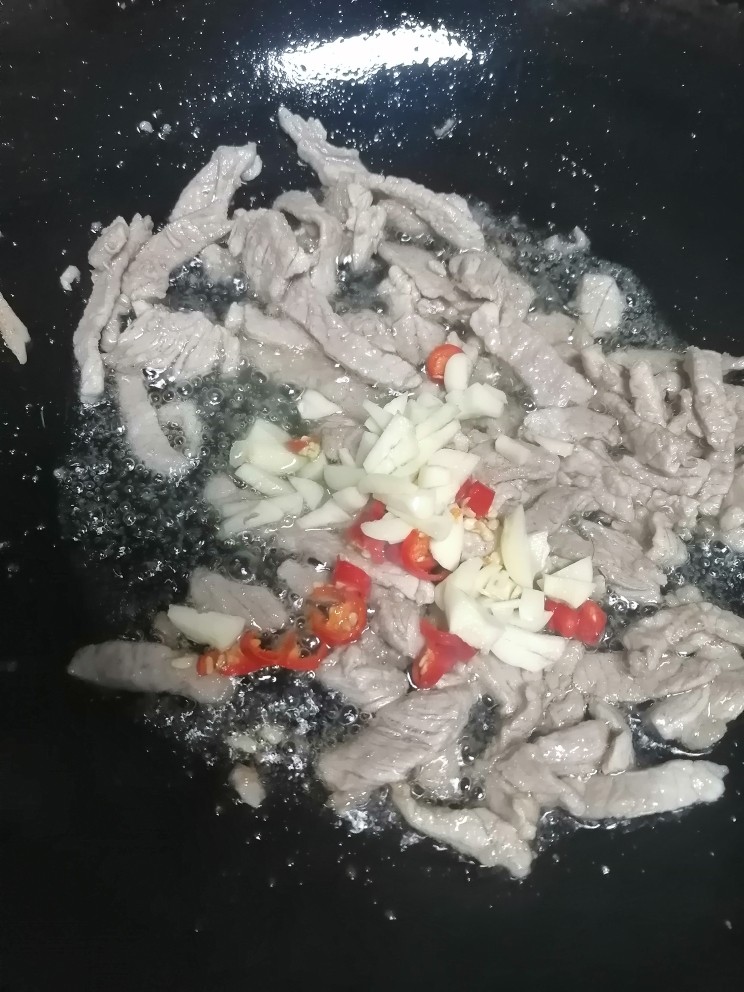 茭白炒肉丝,肉丝两面有些金黄,倒入蒜瓣和辣椒翻炒。