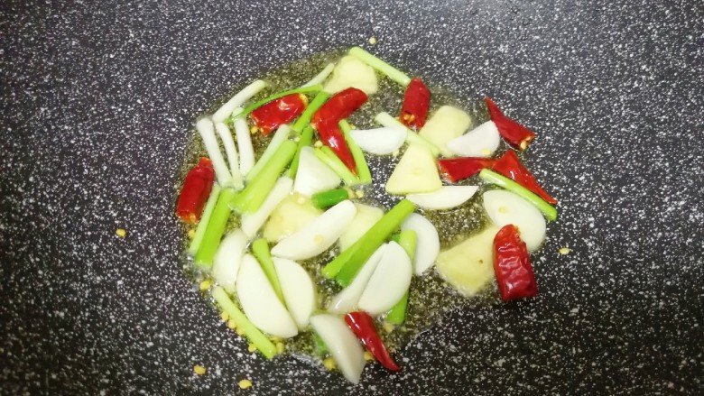 红烧土豆,锅底留余油,下入葱白、蒜片、生姜片和干红辣椒炒香。