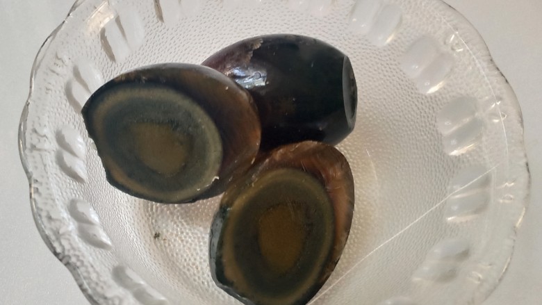 青椒皮蛋,取一根线,拉直,把皮蛋切成四瓣,备用。用线切出来的截面更干净,用刀也可以。