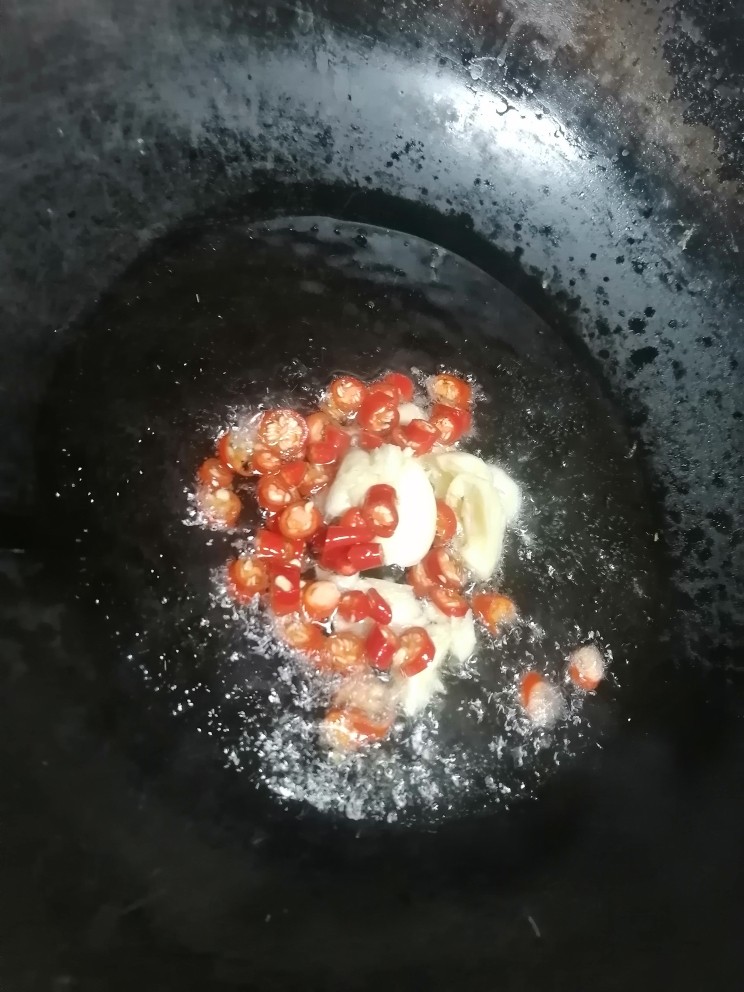 蒜蓉茄子,开火加热锅倒入油,倒入蒜瓣和朝天椒翻炒。