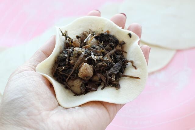 梅干菜肉包,取一张饼皮在中间放适量馅料,然后用右手沿着边缘捏出褶状。