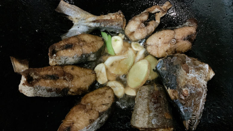 红烧鲅鱼,将锅中煎好的鱼肉移开留出一定空隙,加入姜蒜片、葱白爆香。