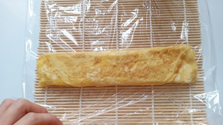 秋葵厚蛋烧,自己吃可以直接切成段了。如果招待客人或者想要成品更完美,准备寿司帘,上面铺上一层保鲜膜,放上厚蛋烧,卷起来,压紧实,定型