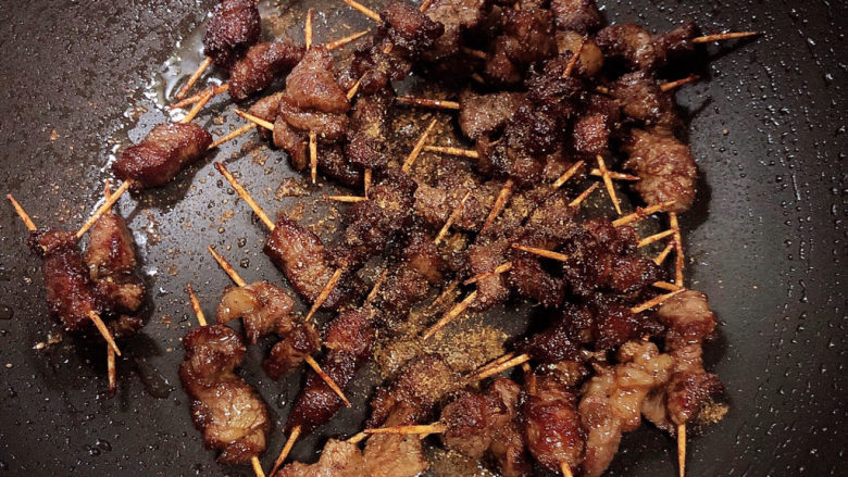 牙签羊肉,锅中倒入少许油,放入炸好的羊肉,撒上花椒粉、孜然粉,超匀出锅。