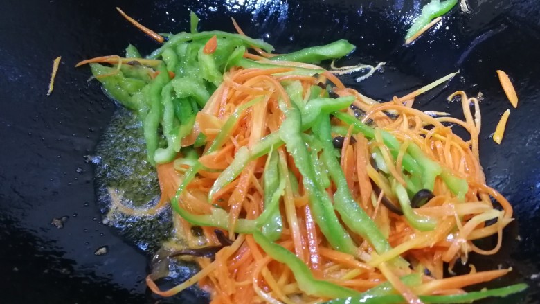 鱼香肉丝,锅里底油先放入胡萝卜丝煸炒均匀，再放尖椒丝文火炒匀。