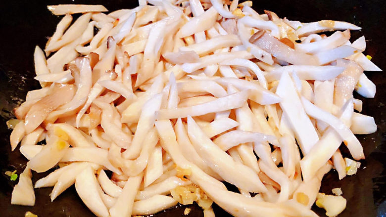青椒炒杏鲍菇,锅中倒入底油加热放入蒜粒爆香再放入杏鲍菇炒匀