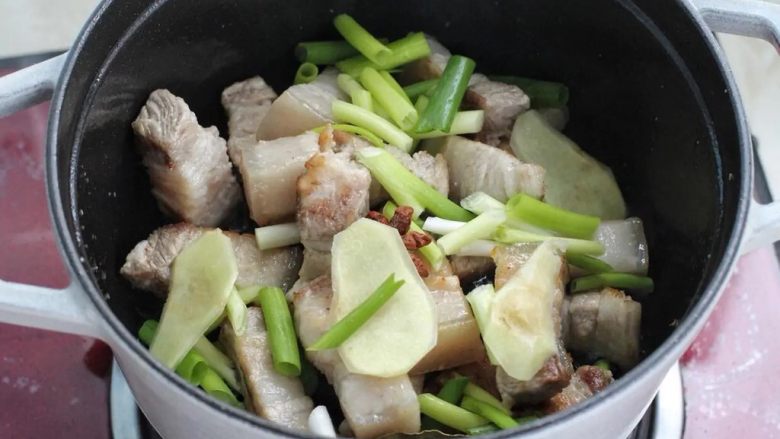 梅干菜烧肉,接着放入冰糖翻炒融化,再放葱段、姜片、八角和香叶炒出香味。