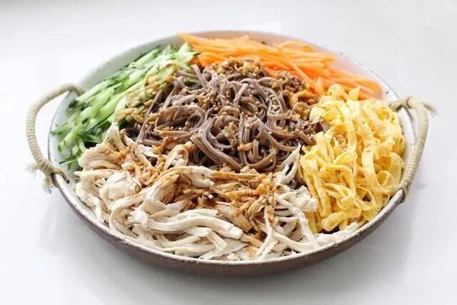 酸辣荞麦面,在荞麦面的旁边依次摆放黄瓜、胡萝卜、鸡蛋皮和鸡胸肉,再将调味汁均匀地淋到上面。