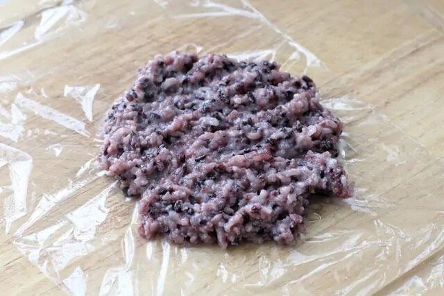 紫米饭团,案板上先铺一层保鲜膜,再舀取适量紫米饭放到上面摊开。