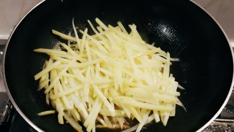 青椒炒土豆丝,锅中留下底油和八角继续加热,放入土豆丝翻炒。