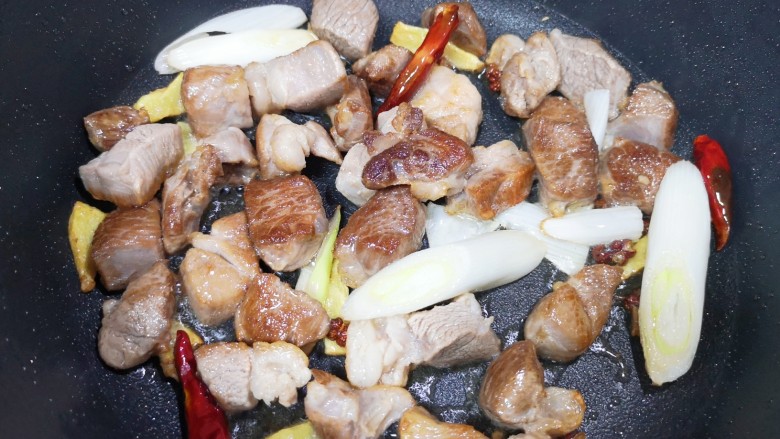 红烧羊肉,下入葱段、干红辣椒和花椒,翻炒至羊肉微微出油。