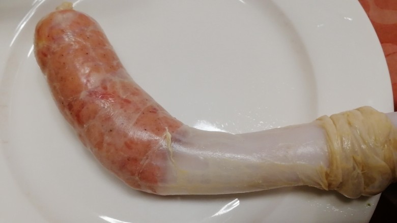 黑胡椒玉米脆皮肠,肠衣套在灌肠口上,顶部打个结,慢慢挤出肉馅。
