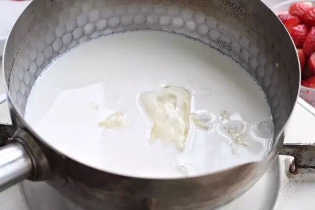 草莓奶冻,把锅坐到炉上开小火,将泡软的吉利丁片放进去,一边煮一边搅拌,使吉利丁片完全溶解在牛奶中。