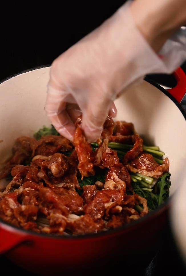 牛肉煲,珐琅锅内倒入油,放入洋葱、姜蒜在底部盖上金针菇、其他青菜,盖上牛肉