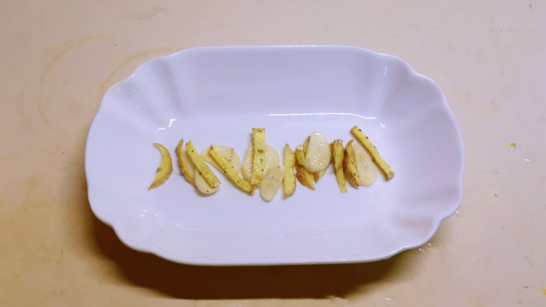 清蒸带鱼,取出鱼盘,将姜丝蒜片铺底。