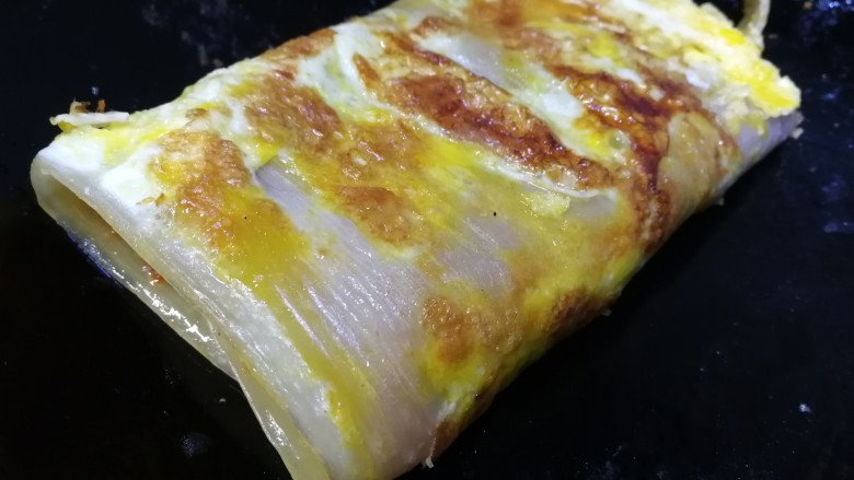 东北烤冷面,卷起,再刷上一层油水,铲子按压煎软。