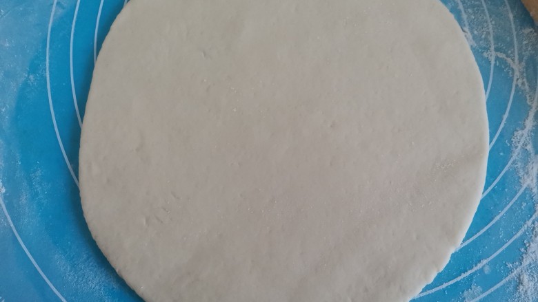 菠萝披萨,把发酵好的面团取出来揉面排气,擀成一个圆饼