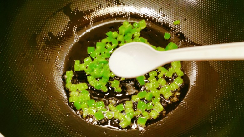 双椒鱼头,利用这个时间,炒锅倒入1汤匙食用油,油热后放入青椒丁翻炒,加入1克盐翻炒断生,关火。