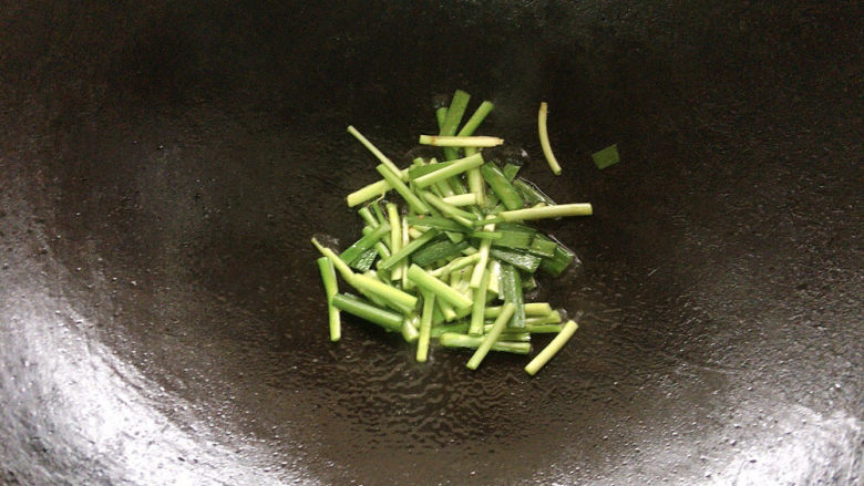 韭菜炒蚕豆,锅烧热油,用韭菜根先行煸炒出香味。
