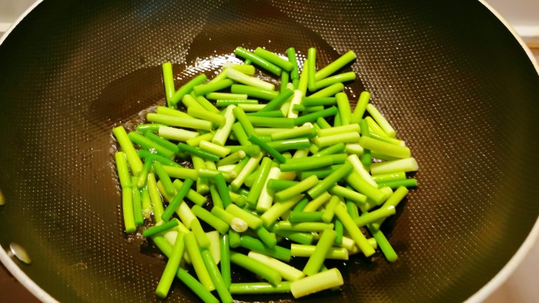 蒜苔炒鱿鱼,起油锅放入1汤匙食用油，油热后放入蒜苔翻炒断生。