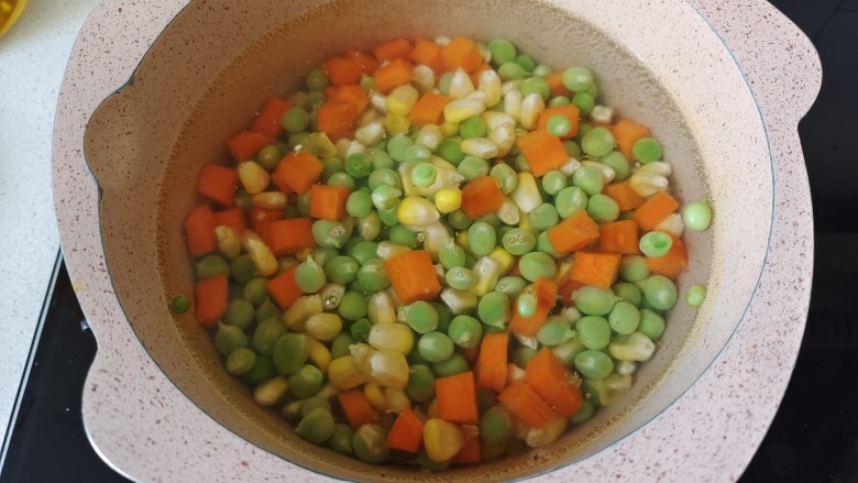 豌豆炒胡萝卜,锅中加入适量清水煮开,倒入胡萝卜丁,豌豆粒,玉米粒焯水2分钟