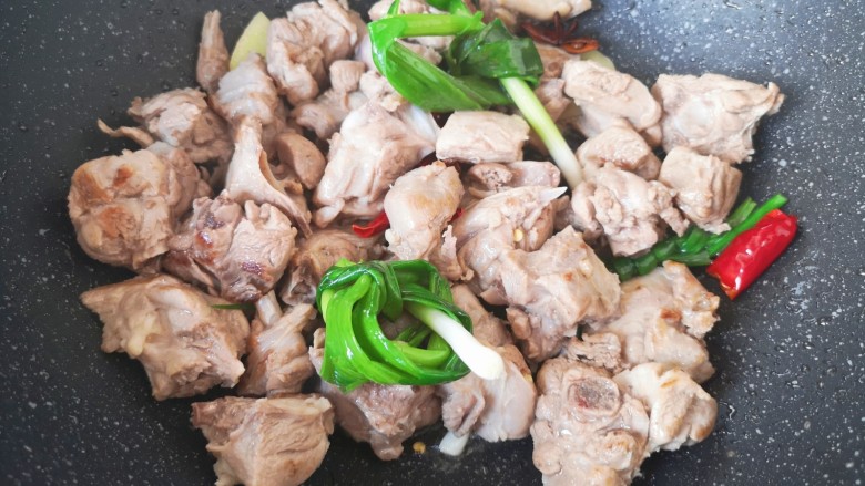 土豆焖鸭,下入小葱结、生姜片、八角、花椒和干红辣椒,炒出香味。