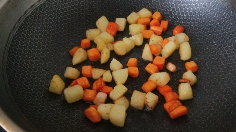 杏鲍菇炒鸡丁,,锅中倒入适量油烧热倒入胡萝卜土豆丁煸炒上色。