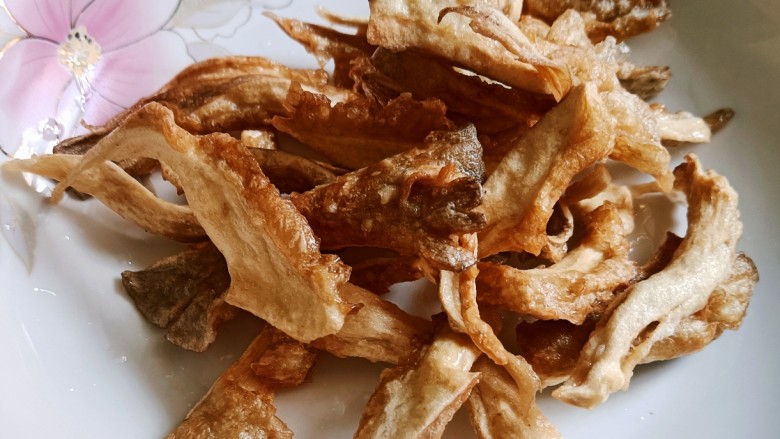 酥炸蘑菇,捞出控油,炸出一锅捞出再炸下一锅。煮一遍炸一遍蘑菇就熟了。这里不需要复炸,复炸的话蘑菇里的水分就炸干了,吃起来就成薯片的口感了,所以炸一遍外酥内软就好了
